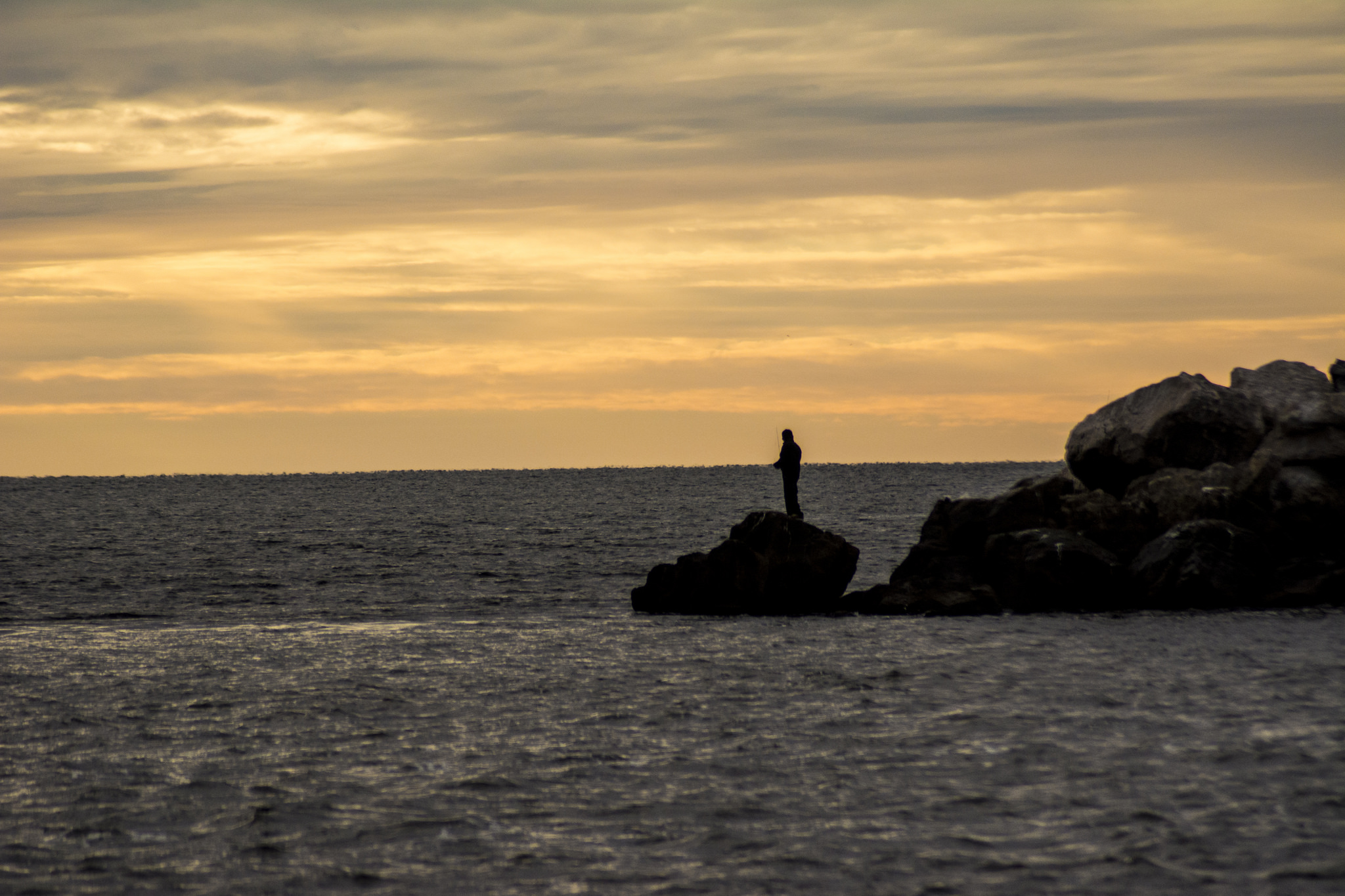 A person standing on a rock in the middle of the ocean