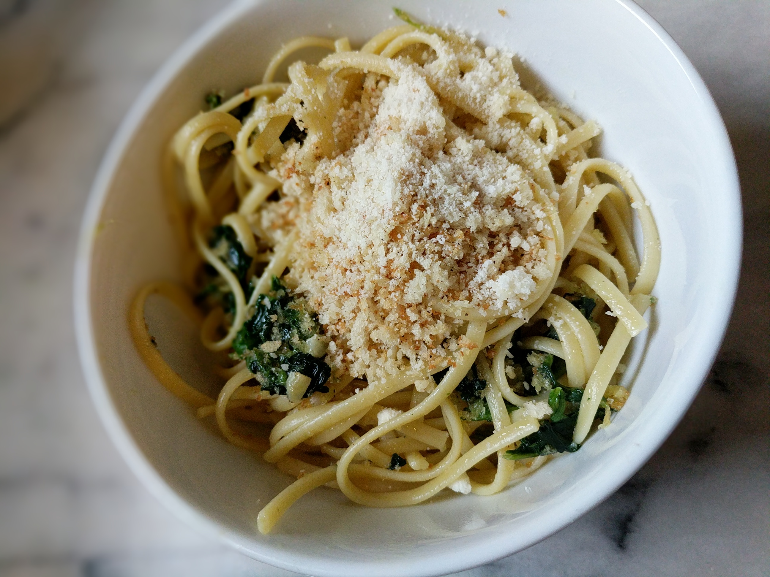 Linguini with spinach, parmesan cheese, and bread cumbs. A prepared dinner in a white bowl.
